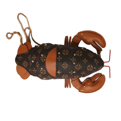 A lobster-shaped handbag featuring Louis Vuitton's classic monogram canvas on the body, brown leather claws and antennae, and small gold-tone studs, shown against a plain white background.
