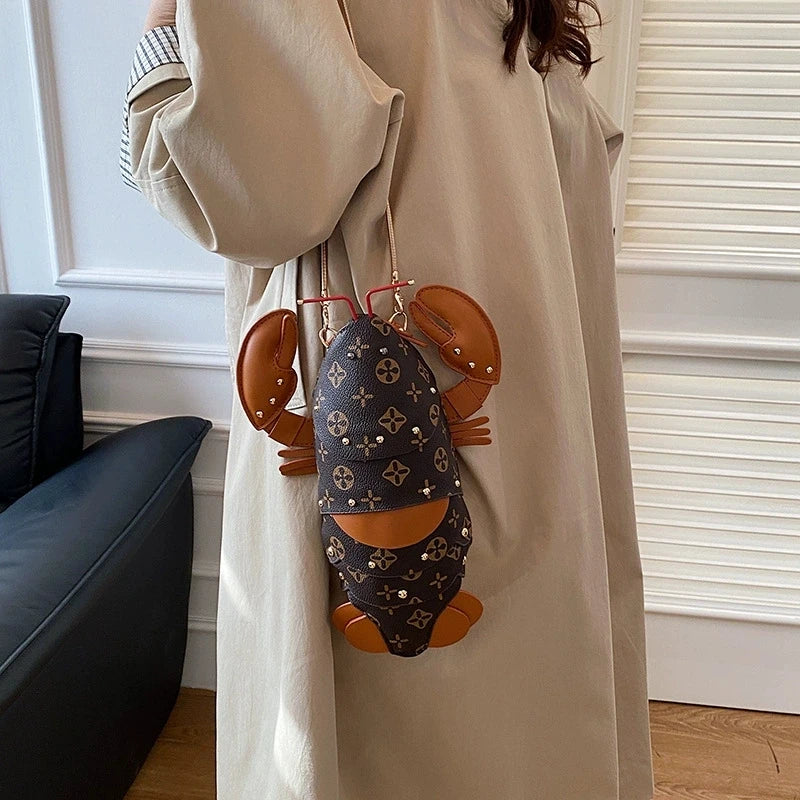 A person wearing a beige trench coat carries a lobster-shaped shoulder bag with a dark brown Louis Vuitton monogram pattern and tan leather claws.