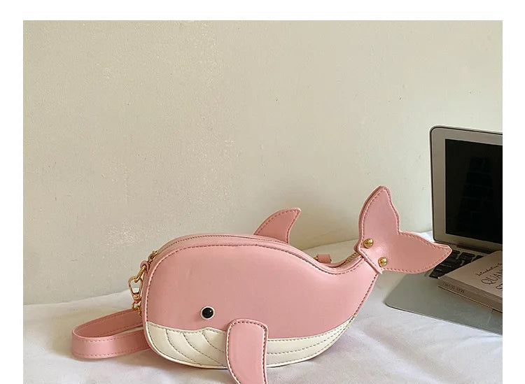 A pink whale-shaped crossbody bag with a cream-colored underside and gold-tone hardware, resting on a white surface next to a laptop. A gray banner at the bottom features Chinese text and the English text 'THE DETAILS SHOW'.