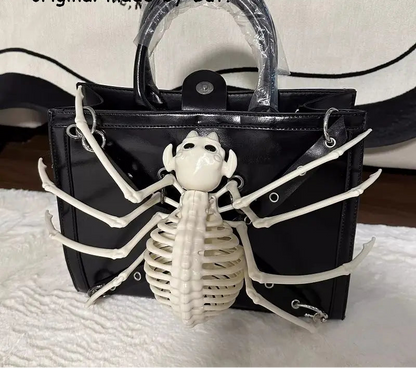 A black patent leather handbag featuring a large white skeleton spider decoration on the front, with a clear plastic-wrapped top handle. The bag is displayed on a white textured surface with a black and white patterned fabric backdrop, and text overlays at the top read 'But Button original made by But.