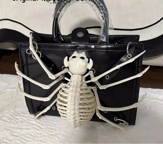 A black patent leather handbag featuring a large white skeleton spider decoration on the front, with a clear plastic-wrapped top handle. The bag is displayed on a white textured surface with a black and white patterned fabric backdrop, and text overlays at the top read 'But Button original made by But.