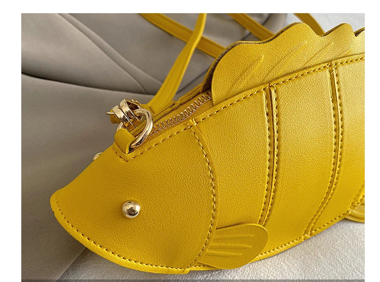 Close-up detail shot of a bright yellow fish-shaped handbag with gold-tone hardware and a zipper, resting on a light gray fabric surface. Chinese text '时尚装饰' and 'THE DETAILS SHOW' appear in a translucent banner at the bottom.