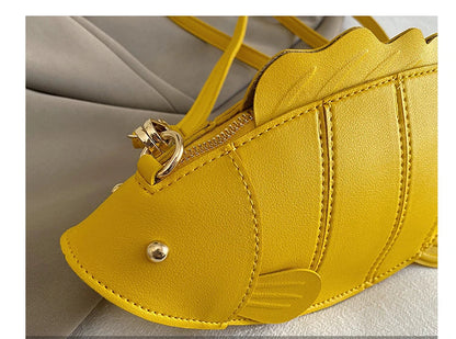 Close-up detail shot of a bright yellow fish-shaped handbag with gold-tone hardware and a zipper, resting on a light gray fabric surface. Chinese text '时尚装饰' and 'THE DETAILS SHOW' appear in a translucent banner at the bottom.