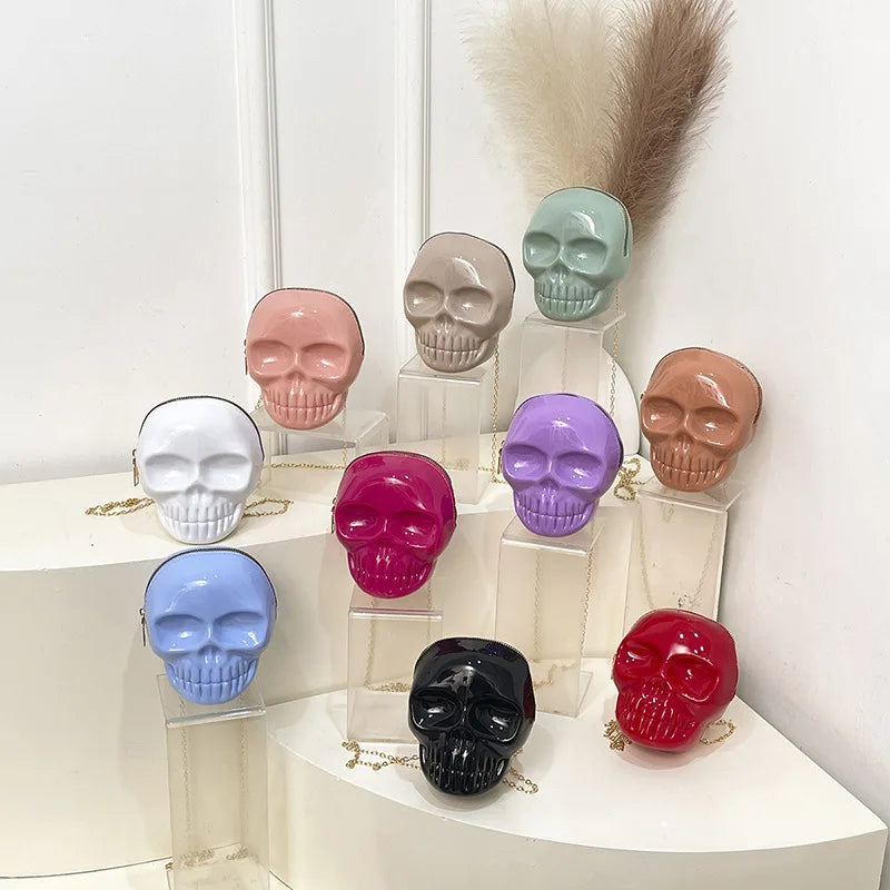 A collection of glossy ceramic skull-shaped handbags in multiple colors, displayed on clear acrylic stands against a white background.