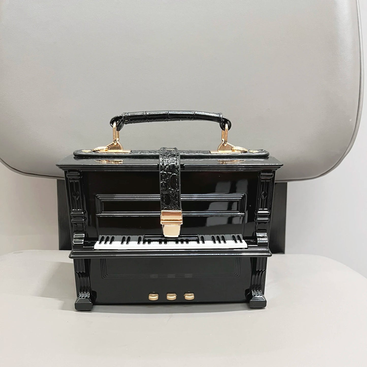 Black and gold piano-shaped handbag on a white surface with a neutral background