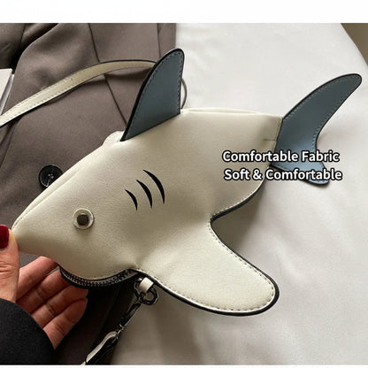 A shark-shaped crossbody bag in off-white faux leather with dark gray accents, held by a hand against a background of a gray blazer and white fabric. Chinese text is overlaid on the right side.