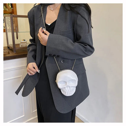 A person wearing a dark gray blazer and black outfit carries a white skull-shaped clutch bag with a silver chain strap.