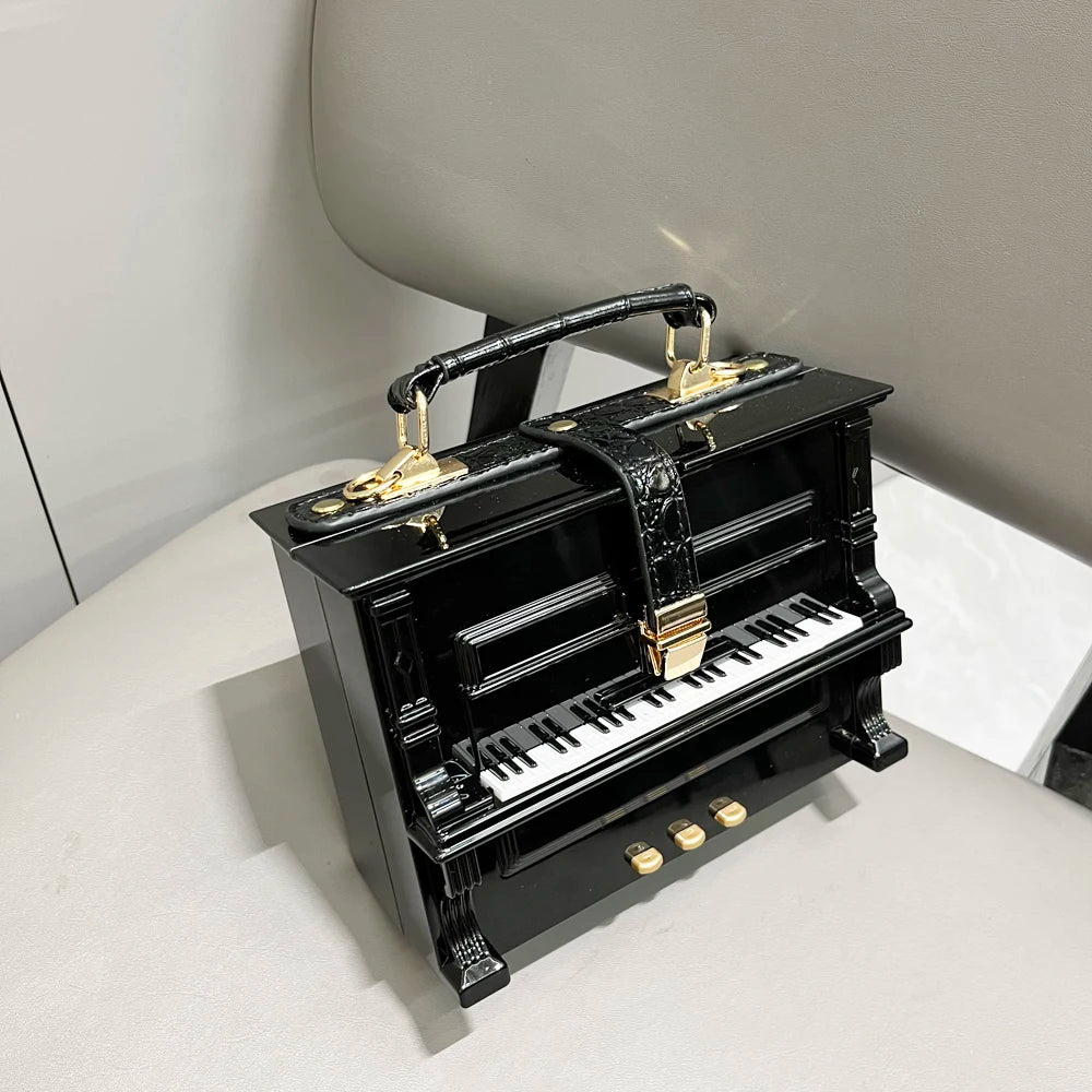 Black piano-shaped handbag with gold accents on a light gray surface.