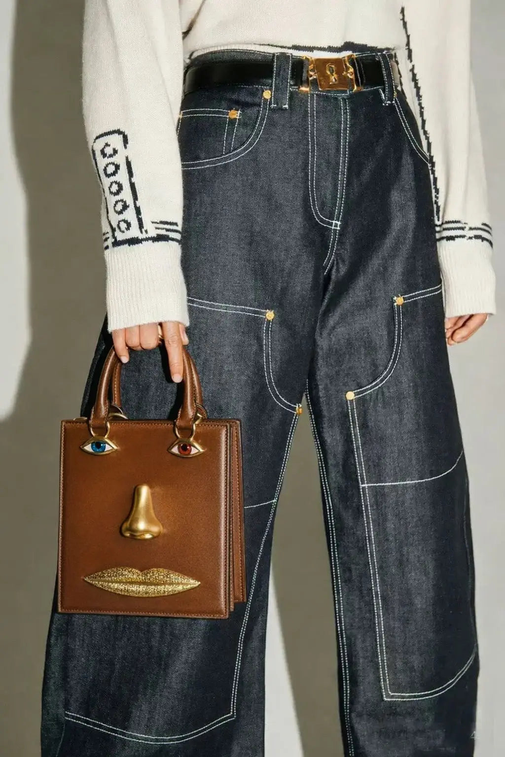 Person wearing high-waisted blue jeans holding a brown handbag with gold accents.