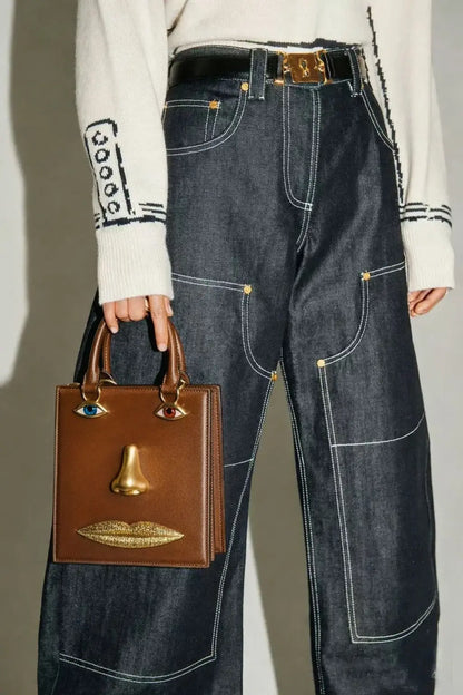 Person wearing high-waisted blue jeans holding a brown handbag with gold accents.